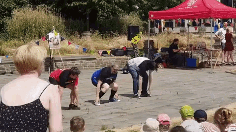 a group of people are squatting down in front of a red tent