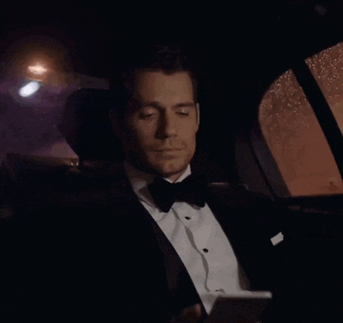 a man in a tuxedo is sitting in the back of a car looking at his phone
