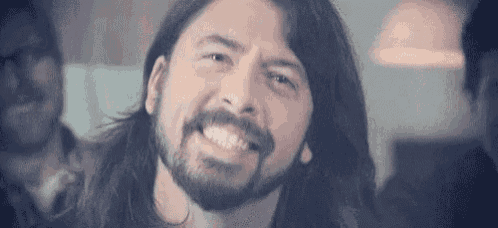 a man with long hair and a beard is smiling at the camera .