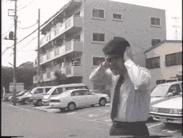 a man in a white shirt and tie covering his ears in front of a building