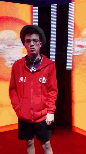 a man wearing a red nice hoodie is standing in front of a large screen .
