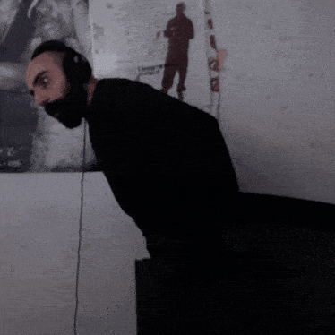 a man wearing headphones stands in front of a wall with a picture of a man from 1995