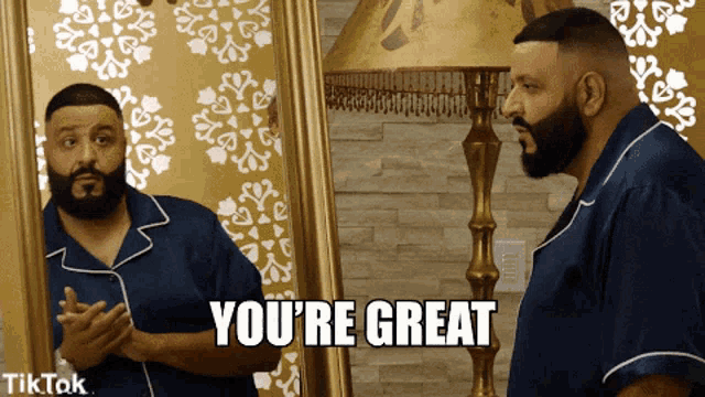 a man with a beard is looking at himself in a mirror and says " you 're great "
