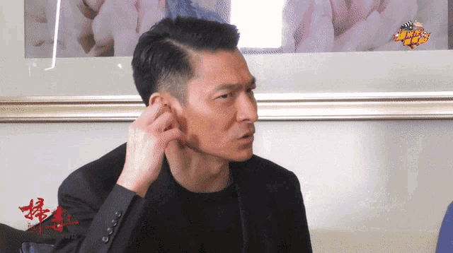 a man in a suit adjusts his ear in front of a framed picture