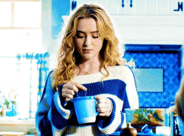 a woman in a blue and white striped sweater is holding a blue mug of coffee .