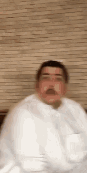 a man with a mustache is wrapped in a white blanket and is making a funny face .
