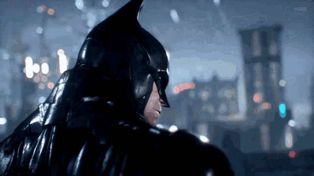 a man in a batman costume stands in front of a blurry cityscape