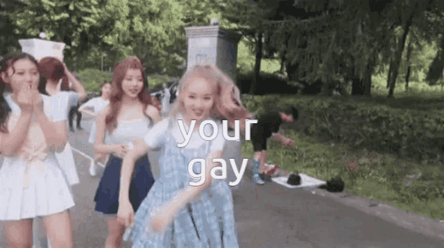 a group of girls are walking down a street with the words your gay written on the bottom .