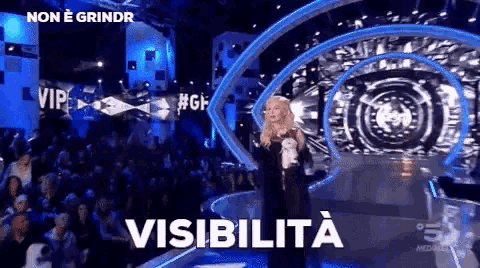 a woman is standing on a stage in front of a crowd and the word visibilita is on the screen
