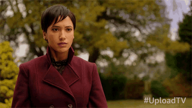 a woman in a burgundy coat stands in front of trees with the hashtag uploadtv