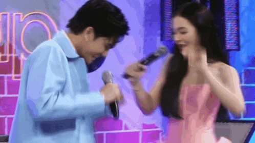 a man and a woman are standing next to each other holding microphones . the woman is wearing a pink dress .