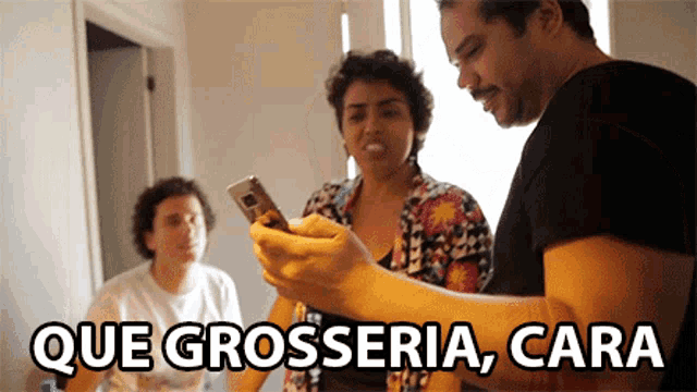a group of people looking at a cell phone with the words que grosseria cara on the bottom right