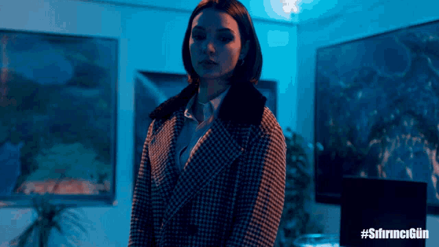 a woman in a plaid coat stands in a room with a sign that says #sihrncigun on it