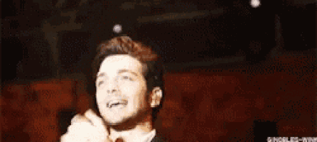 a man in a suit and tie is standing in front of a microphone in an auditorium .