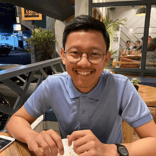 a man wearing glasses is sitting at a table in front of a sign that says ' cook ' on it