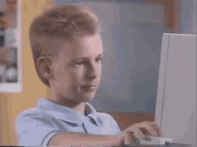 a young boy is sitting in front of a laptop computer and typing on it .