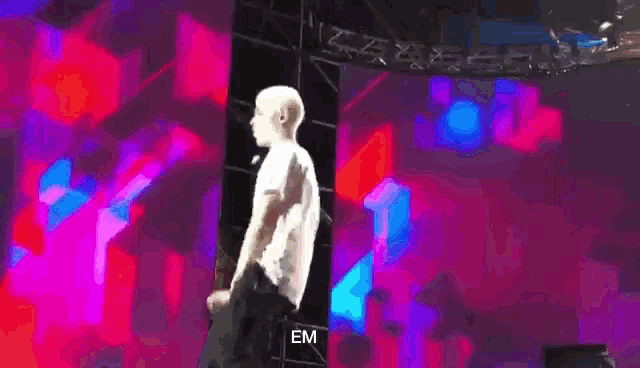 a man in a white shirt is standing on a stage with the word em on the bottom right