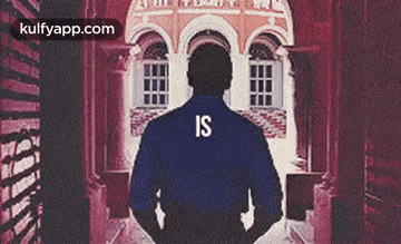 a man wearing a blue shirt with the word is on the back is standing in a hallway .