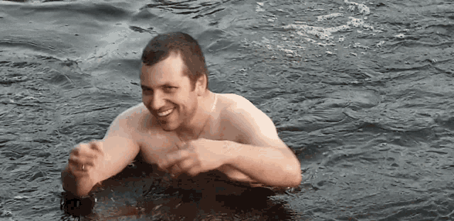 a man without a shirt is swimming in the water and smiling