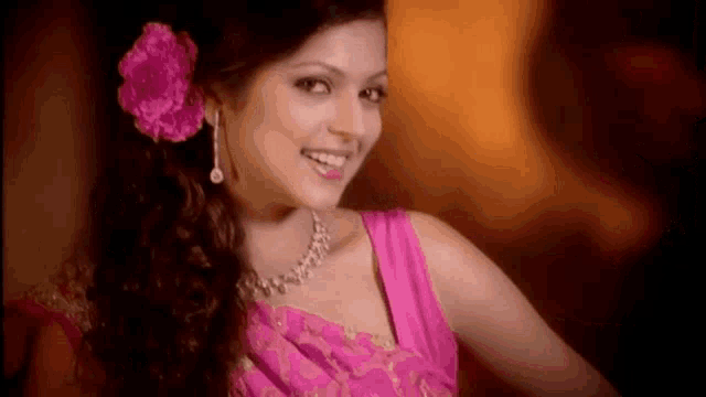 a woman wearing a pink dress and a pink flower in her hair is smiling .