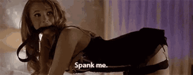 a woman in lingerie is laying on her stomach on a bed and holding a leash in her mouth .