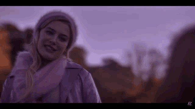 a woman in a pink coat and hat is standing in a field .