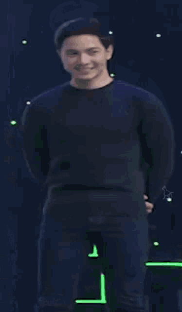 a man in a black shirt is smiling and holding his hands in his pockets .