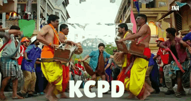 a group of men are dancing on a street and the word kcpd is on the bottom right
