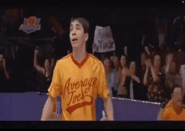 a man wearing a yellow shirt that says average joes is standing in front of a crowd .