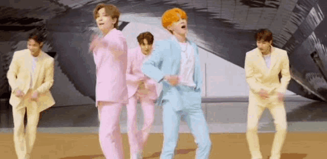 a group of men in pink and yellow suits are dancing on a stage .