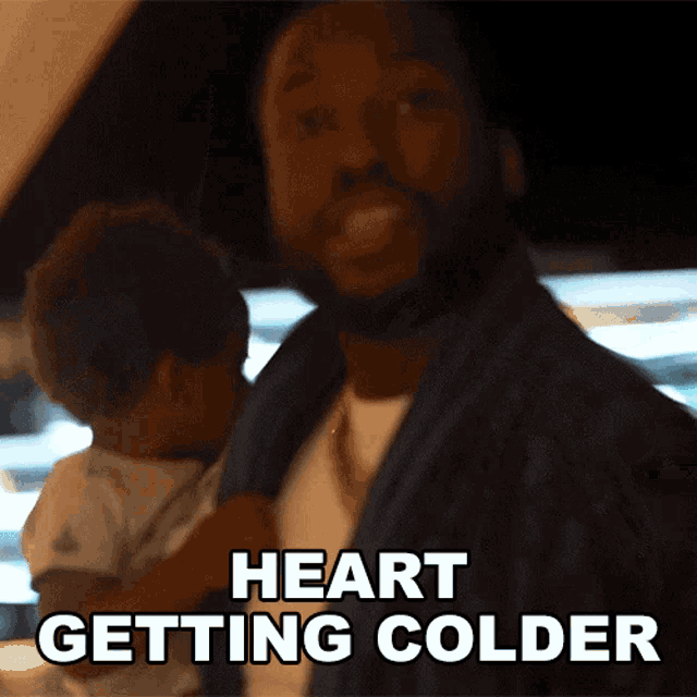 a man is holding a baby and the words heart getting colder are above him
