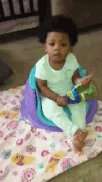 a baby is sitting on a blanket with a toy