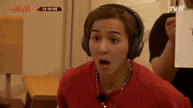 a man wearing headphones looks surprised while holding a piece of paper that says tvn