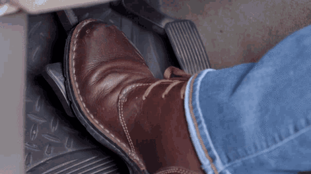 a person wearing a pair of brown boots is pressing the brake pedal