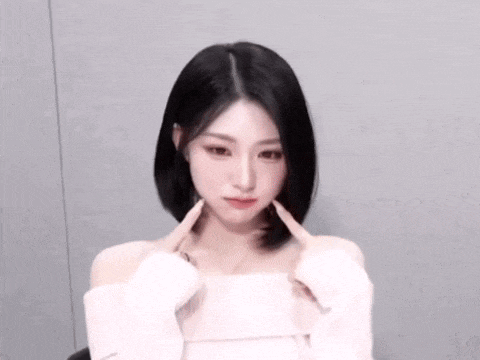 the woman is wearing a white off the shoulder top and making a heart shape with her hands .