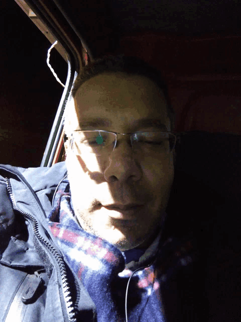 a man wearing glasses and a plaid scarf is sitting in a car