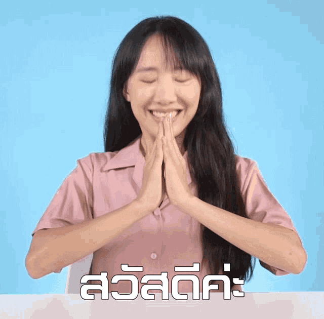 a woman in a pink shirt is smiling with her hands folded in front of a blue background that says สวัสดี คะ