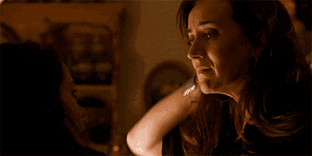 a woman in a black shirt is talking to a man in a dark room