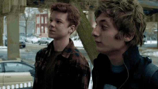two young men are standing next to each other on a street looking up