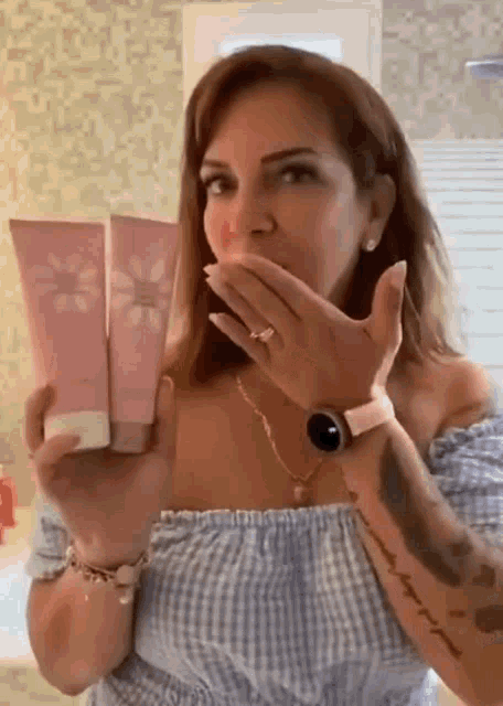 a woman is holding two bottles of lotion in her hands and covering her mouth .