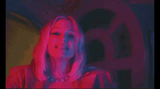 a woman with a ring on her finger looks at the camera with red and blue lights behind her
