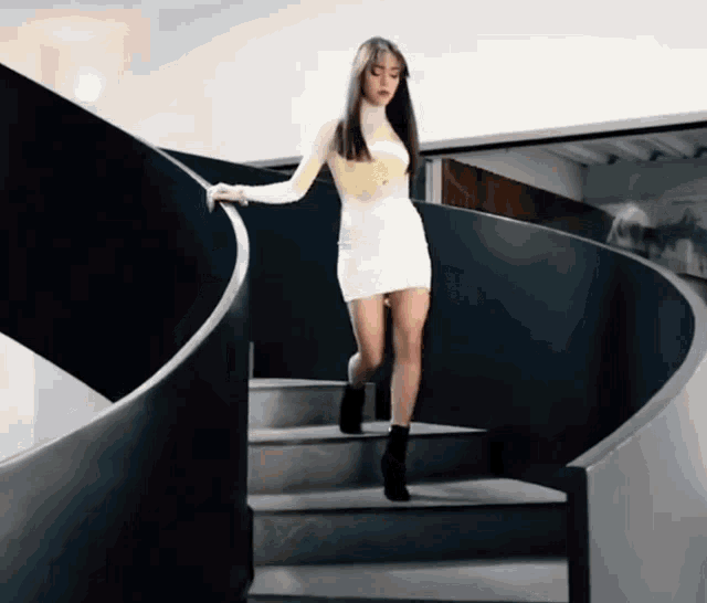 a woman in a white dress is walking down a set of spiral stairs