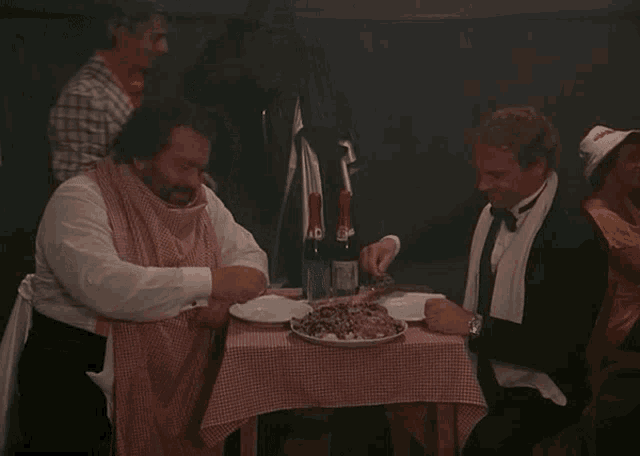 a man in a tuxedo sits at a table with a plate of food and a bottle of wine