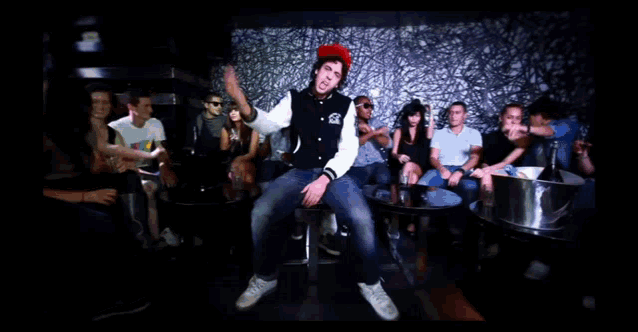 a man wearing a red hat with a yellow sticker on it is surrounded by women dancing