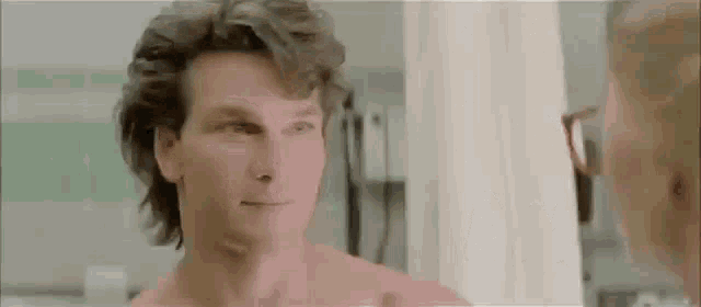 a shirtless man is looking at himself in the mirror in a hospital room .