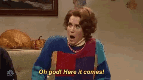 a woman in a colorful sweater is sitting at a table with a surprised look on her face .