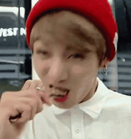 a young man wearing a red beanie and a white shirt is eating something .
