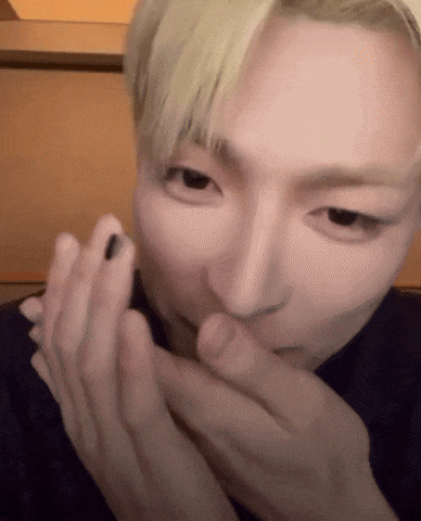 a man with blonde hair is applying black nail polish to his nails .