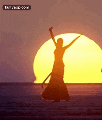 a woman is dancing on the beach in front of the sun at sunset .