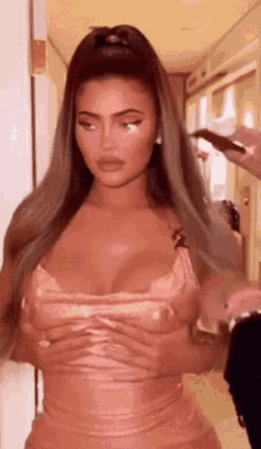 a woman in a pink dress is standing in a hallway with her hands on her breasts .